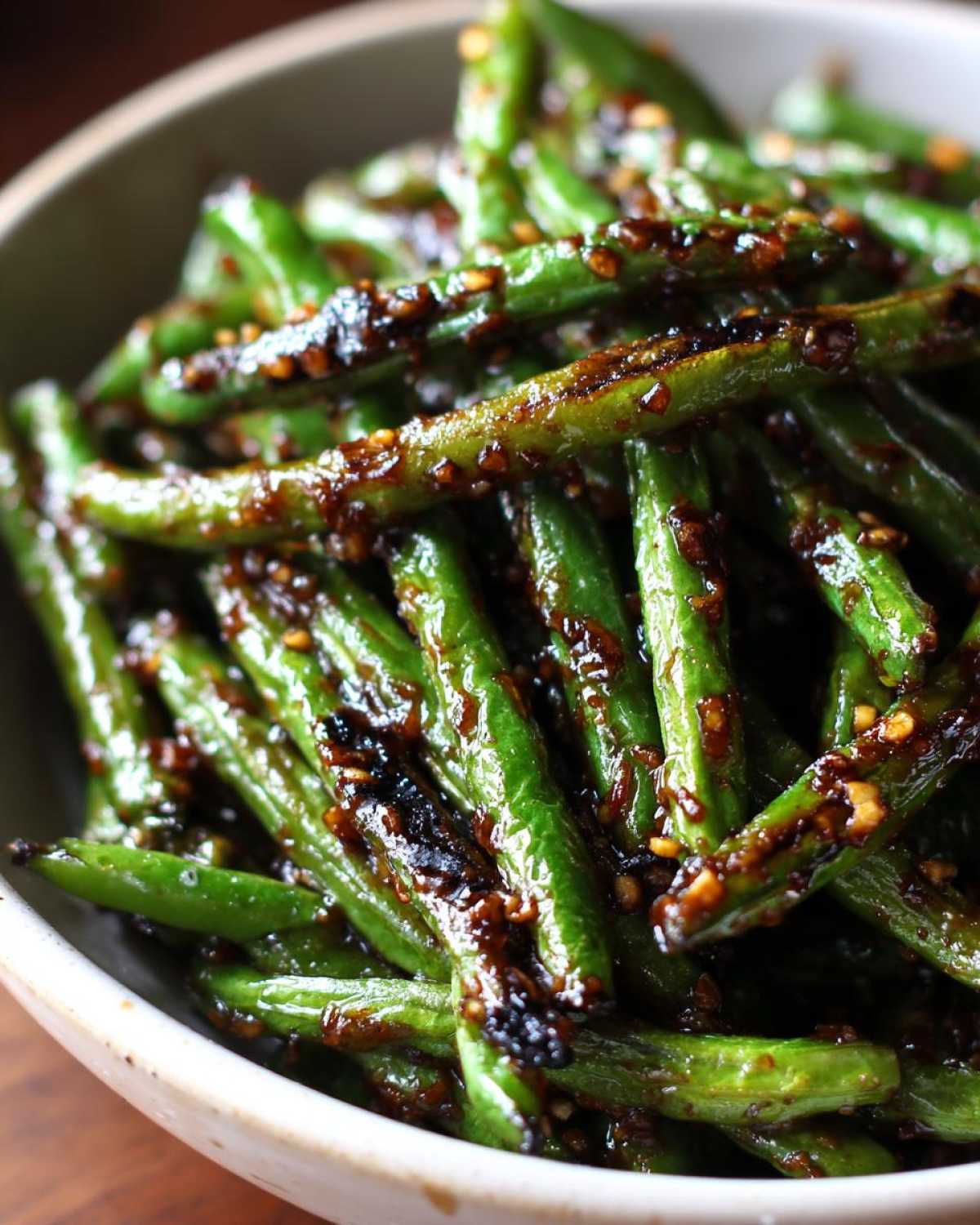 Close-up of bright green, blistered chinese green beans with garlic sauce coating and sesame seeds.