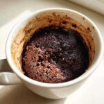 Close-up of a rich, dark chocolate mug cake topped with mini chocolate chips inside a white mug.