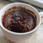 Close-up of a freshly baked chocolate mug cake in a white mug, topped with chocolate chips.
