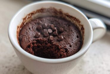 Close-up of a freshly baked chocolate mug cake in a white mug, topped with chocolate chips.