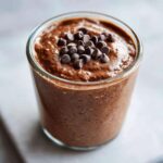 Close-up of rich chocolate overnight oats in a glass, topped with mini chocolate chips.