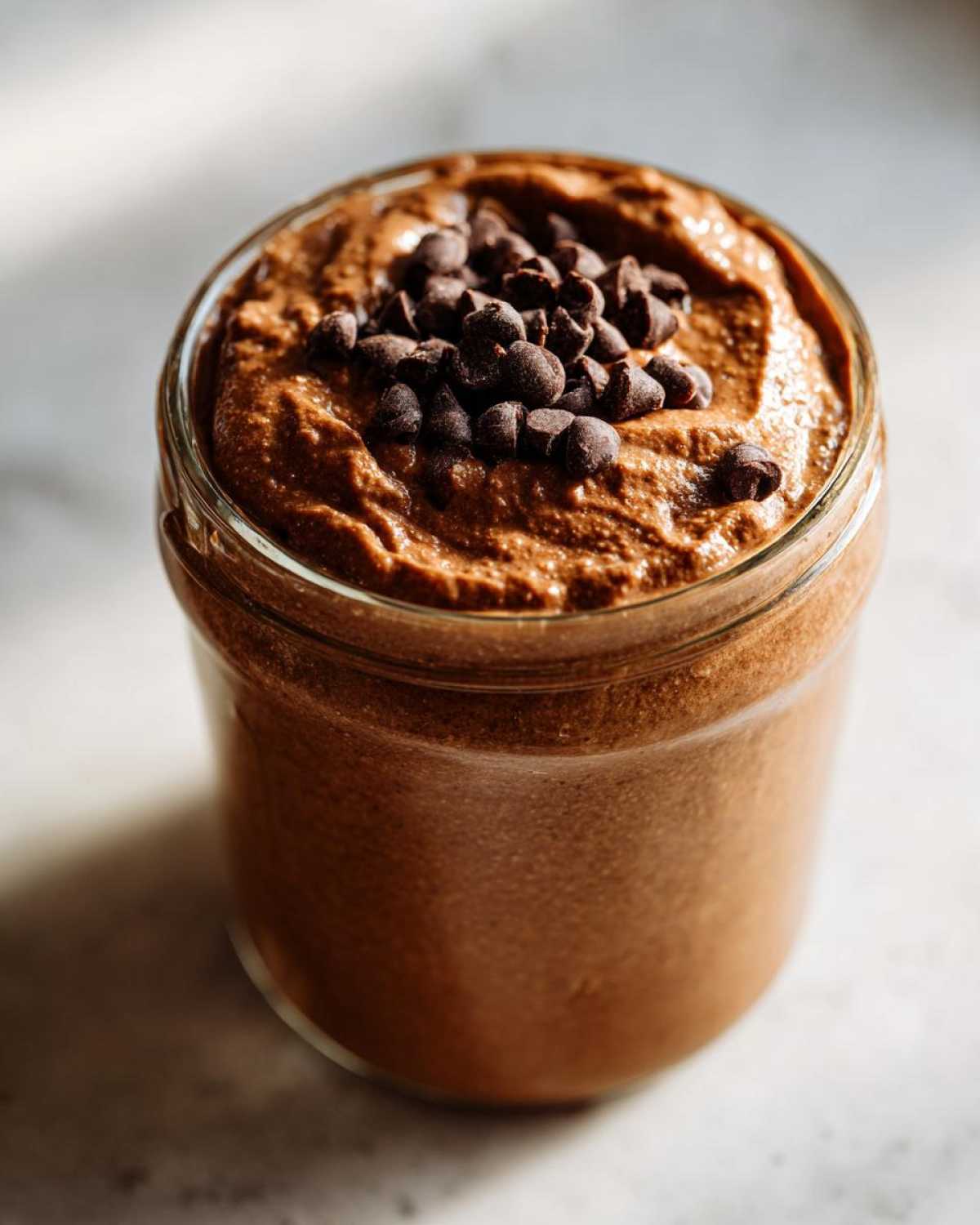Close-up of thick chocolate overnight oats in a glass jar, topped generously with mini chocolate chips.