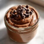 Close-up of creamy chocolate overnight oats in a glass jar, topped generously with mini chocolate chips.
