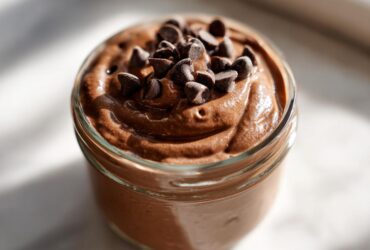 Close-up of creamy chocolate overnight oats in a glass jar, topped generously with mini chocolate chips.