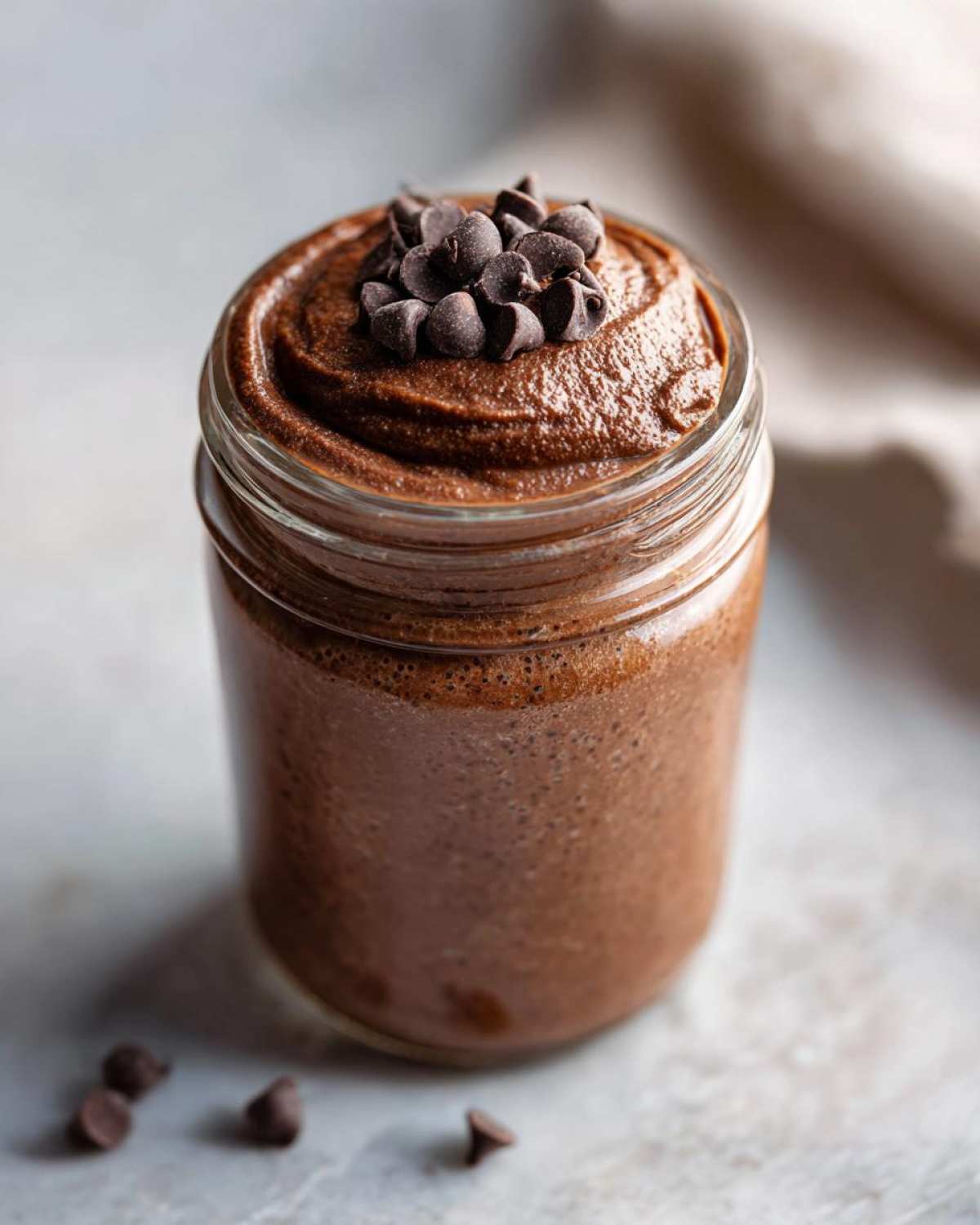 A close-up of creamy chocolate overnight oats topped with chocolate chips in a glass jar.