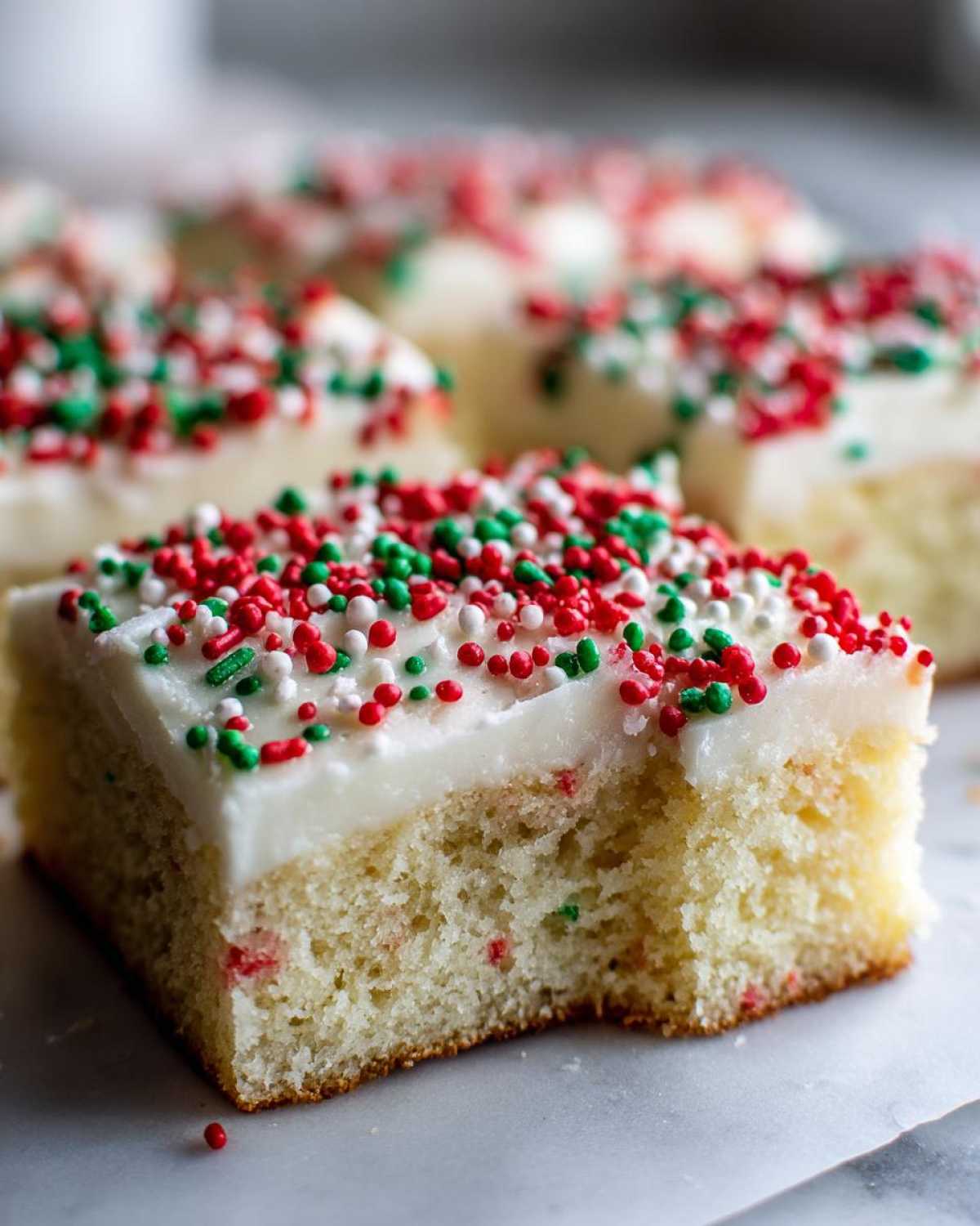 A square piece of soft christmas sugar cookie bars topped with white frosting and red, green, and white sprinkles.