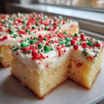 A close-up of a square slice of christmas sugar cookie bars topped with white frosting and festive red and green sprinkles.