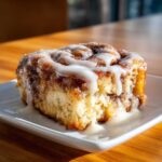 Close-up of a single, decadent serving of Cinnamon roll casserole topped with thick white icing.