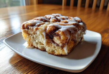 A close-up of a warm slice of cinnamon roll casserole topped generously with white icing.
