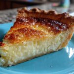 A close-up of a slice of classic buttermilk pie featuring a creamy filling and a deeply browned, caramelized top crust.