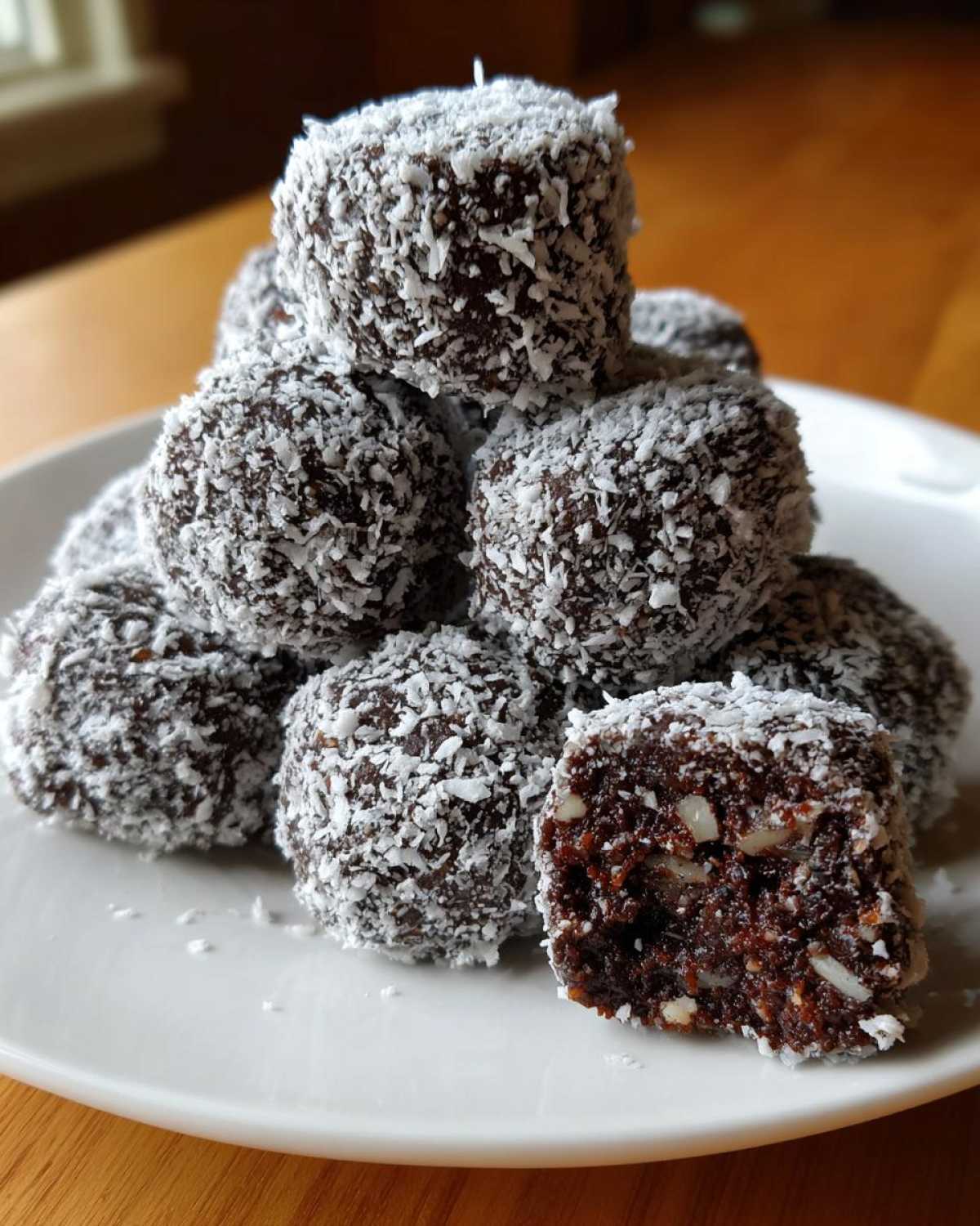 A stack of dark chocolate bourbon balls rolled in shredded coconut, with one cut open showing nuts inside.