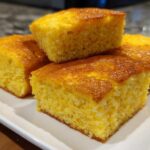 Four golden squares of moist cornbread stacked on a white plate, perfect alongside sheet pan eggs.