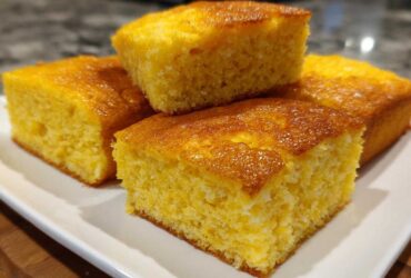 Four golden squares of moist cornbread stacked on a white plate, perfect alongside sheet pan eggs.