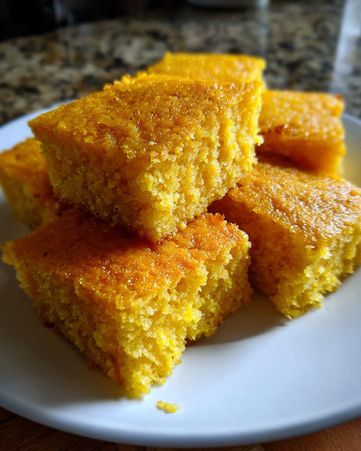 Close-up of golden, moist cornbread squares stacked on a white plate, a side dish for sheet pan eggs.