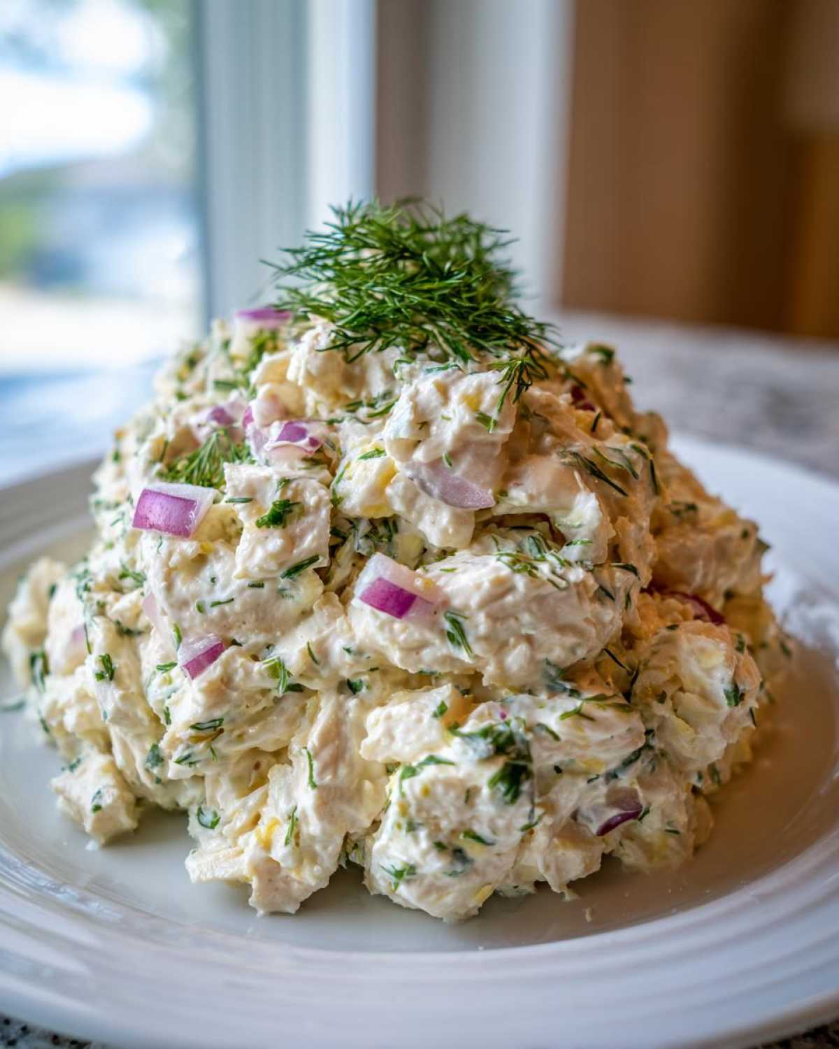 A mound of creamy cottage cheese chicken salad mixed with red onion and topped with fresh dill.