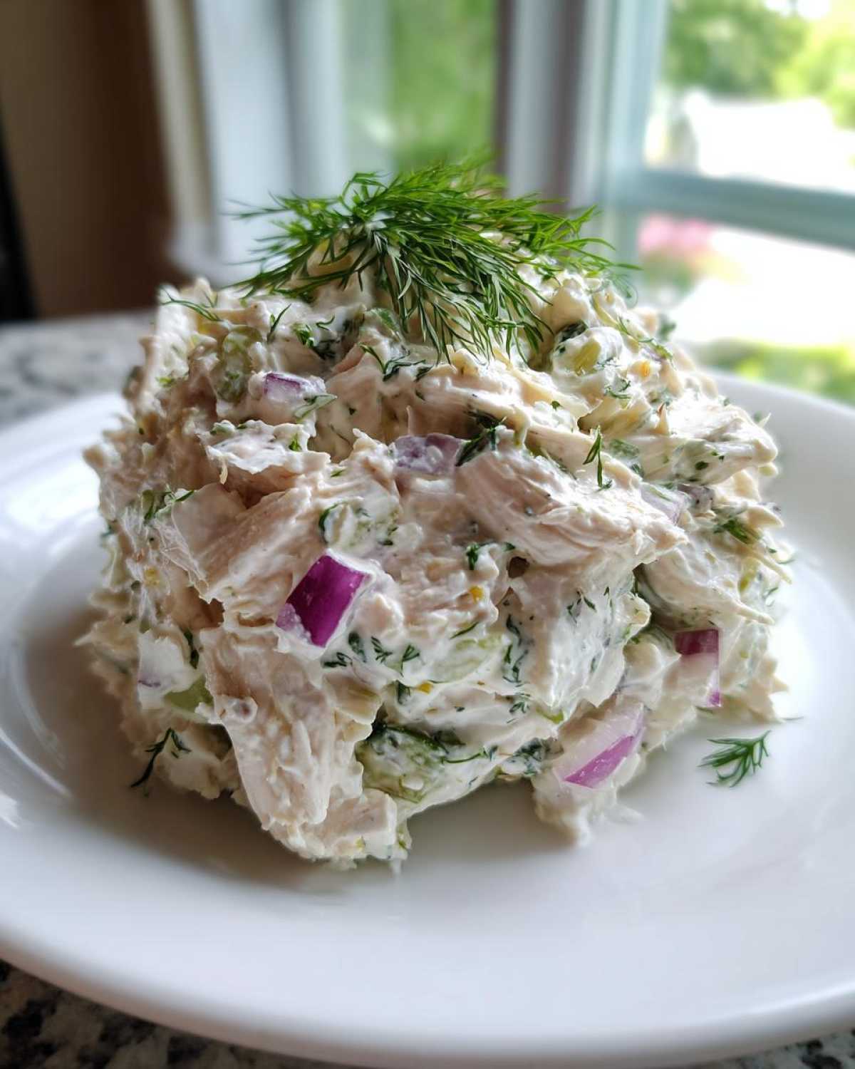 A scoop of creamy cottage cheese chicken salad mixed with red onion and topped with fresh dill.