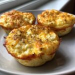 Three freshly baked cottage cheese egg cups starbucks style, topped with melted cheese and dried herbs on a light plate.