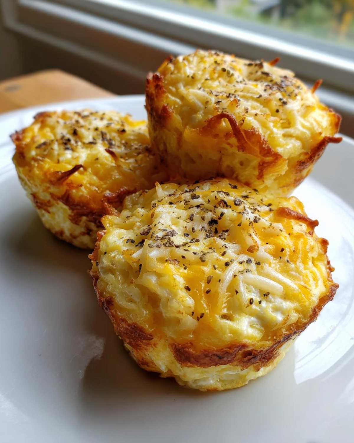 Three golden-brown cottage cheese egg cups topped with melted cheese and herbs on a white plate.
