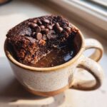 A close-up of a rich, dark Cottage Cheese Microwave Brownie in a speckled mug, topped with melted chocolate chips.