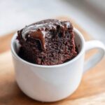 A rich, dark slice of Cottage Cheese Microwave Brownie topped with dripping chocolate sauce, served in a white mug.