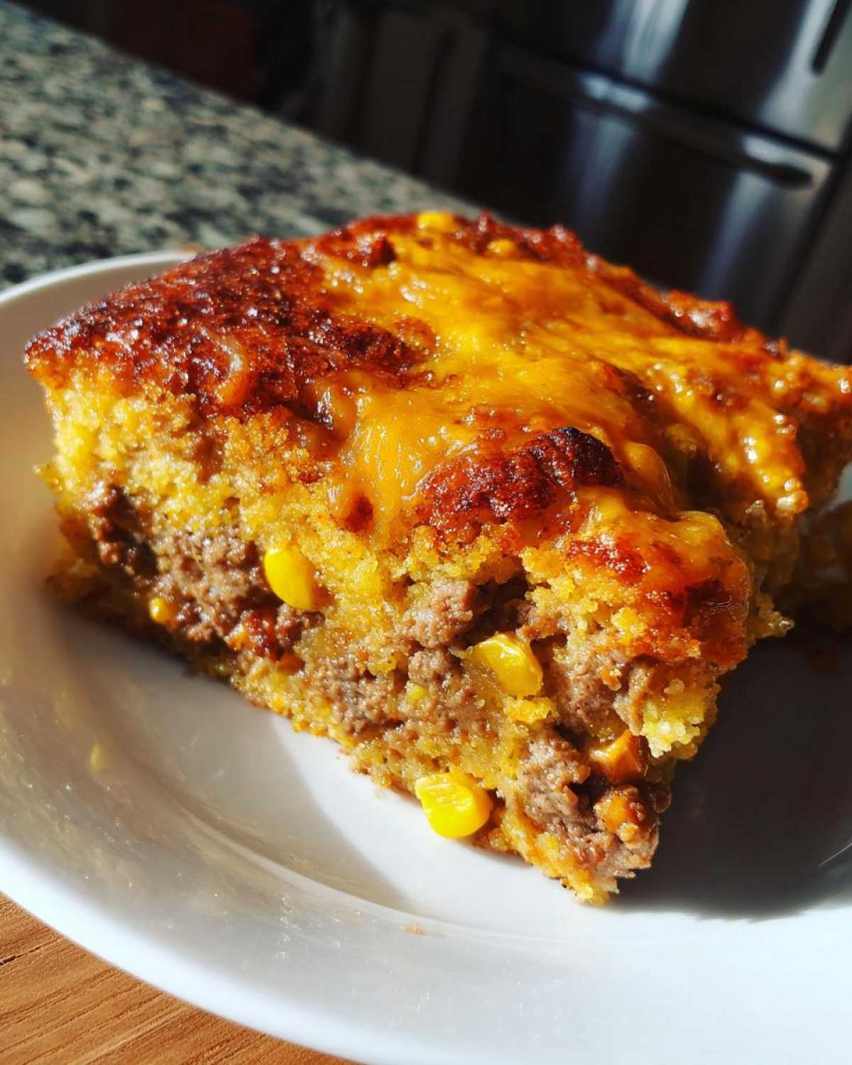 Close-up of a square slice of cowboy cornbread casserole with ground meat, corn, and melted cheddar cheese topping.