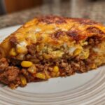 Close-up of a hearty slice of cowboy cornbread casserole showing layers of seasoned ground beef, corn, and cheesy topping.