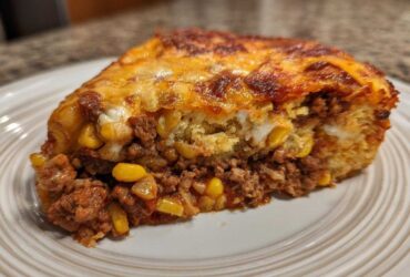 Close-up of a hearty slice of cowboy cornbread casserole showing layers of seasoned ground beef, corn, and cheesy topping.