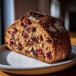 A close-up of a freshly baked cranberry walnut bread loaf showing a rich interior filled with dried cranberries and walnuts.