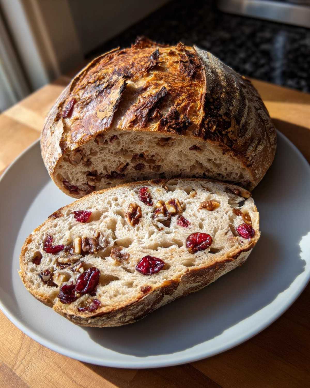 A loaf of cranberry walnut bread, sliced open to show cranberries and walnuts inside, resting on a plate.