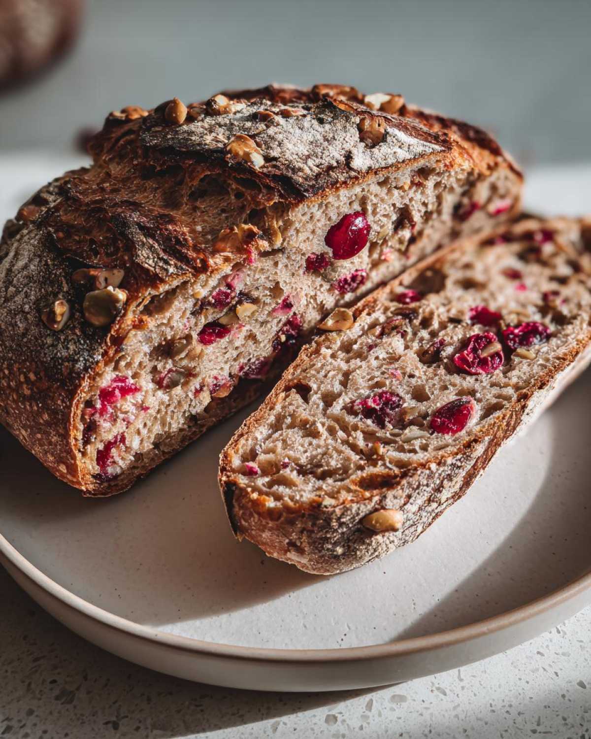 A rustic loaf of cranberry walnut bread, sliced open to show dried cranberries and walnuts inside.