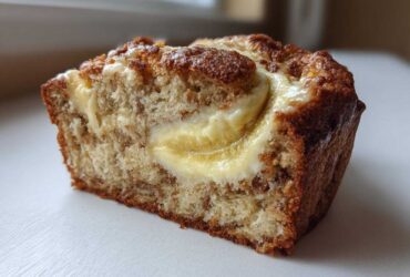 Close-up of a slice of moist cream cheese banana bread showing a rich cream cheese swirl.