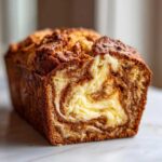 A close-up of a baked cream cheese banana bread loaf showing a rich swirl of cream cheese filling inside the bread.