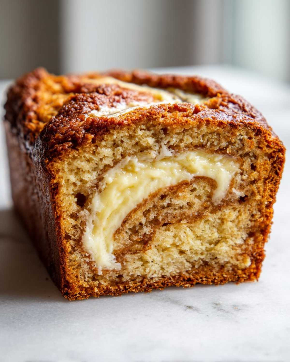 Close-up of a golden brown cream cheese banana bread loaf showing a swirl of creamy filling inside.