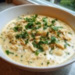 A close-up of a bowl of rich, creamy cream cheese chicken chili loaded with shredded chicken and fresh parsley.