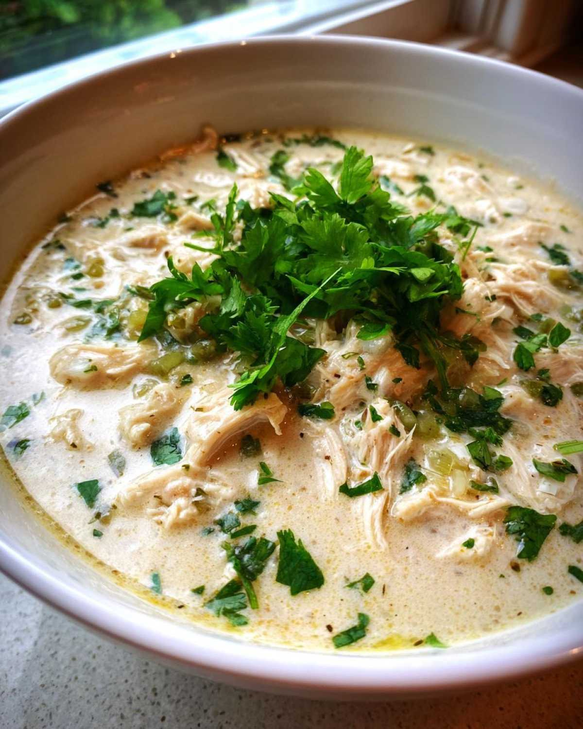 Close-up of creamy white cream cheese chicken chili topped with fresh parsley.