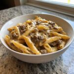 A close-up of creamy beef pasta made with penne noodles and ground beef, served in a white bowl.