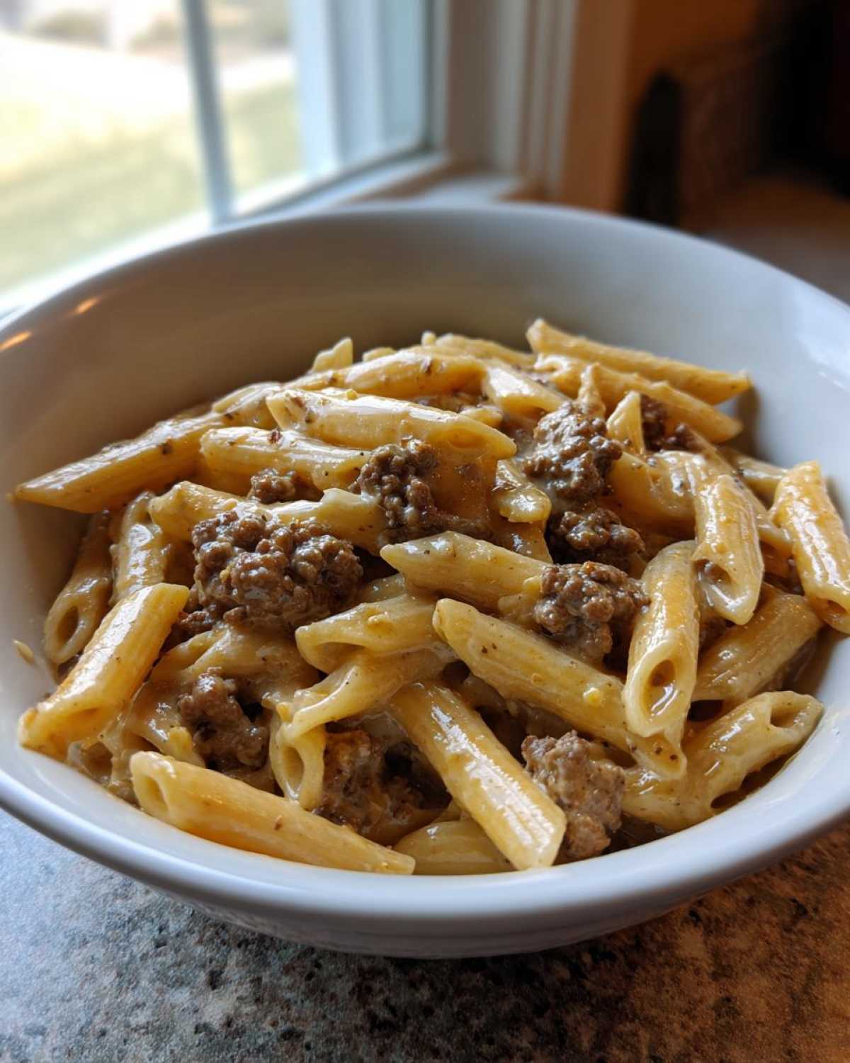 A close-up shot of creamy beef pasta made with penne noodles and seasoned ground beef in a white bowl.