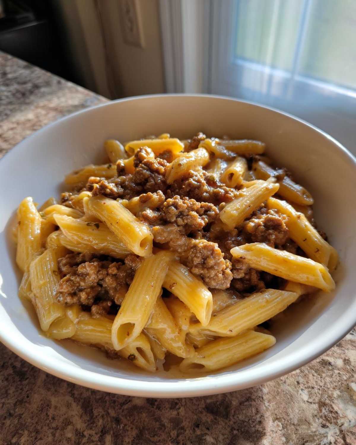 A close-up of creamy beef pasta made with penne noodles and ground beef in a white bowl.