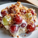 A close-up of a serving of creamy chicken salad chick grape salad, featuring red and green grapes coated in dressing and topped with crunchy pecans.