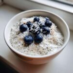 A close-up of creamy coconut chia pudding topped with fresh blueberries and shredded coconut.