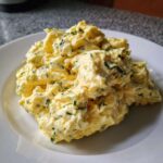 A mound of creamy, yellow egg salad recipe mixed with finely chopped green herbs, served on a white plate.
