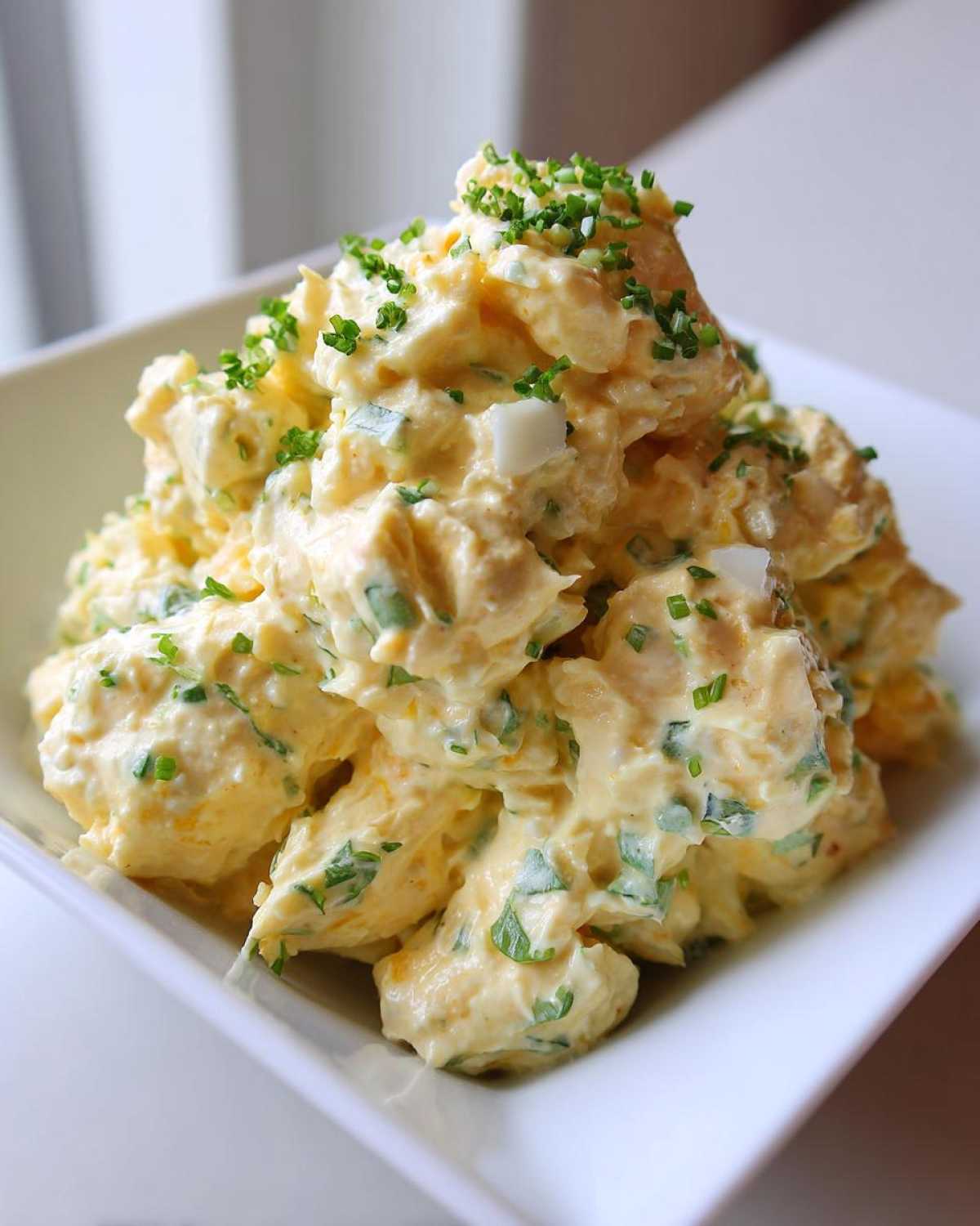 A mound of creamy, rich egg salad recipe garnished generously with freshly chopped green chives in a white bowl.
