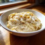 A white bowl filled with fettuccine pasta coated in rich homemade alfredo sauce and topped with black pepper.