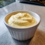 Close-up of thick, creamy yellow garlic aioli served in a small white fluted ramekin.