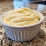 Close-up of rich, creamy garlic aioli swirled high in a small white fluted ramekin.