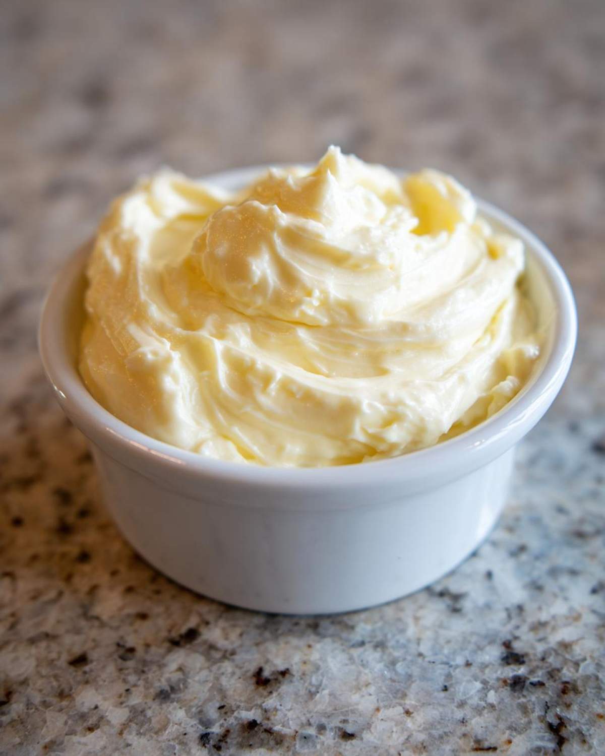 A close-up of rich, creamy garlic aioli swirled beautifully in a small white bowl.