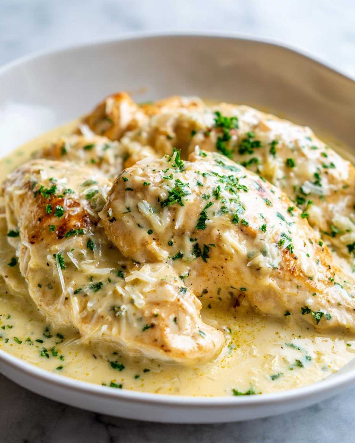 Three golden chicken breasts smothered in a rich, creamy lemon sauce and topped with grated cheese and parsley.