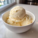 Close-up of three scoops of pale yellow, creamy protein ice cream served in a white bowl.