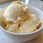 Two scoops of creamy, pale yellow protein ice cream served in a small white bowl.