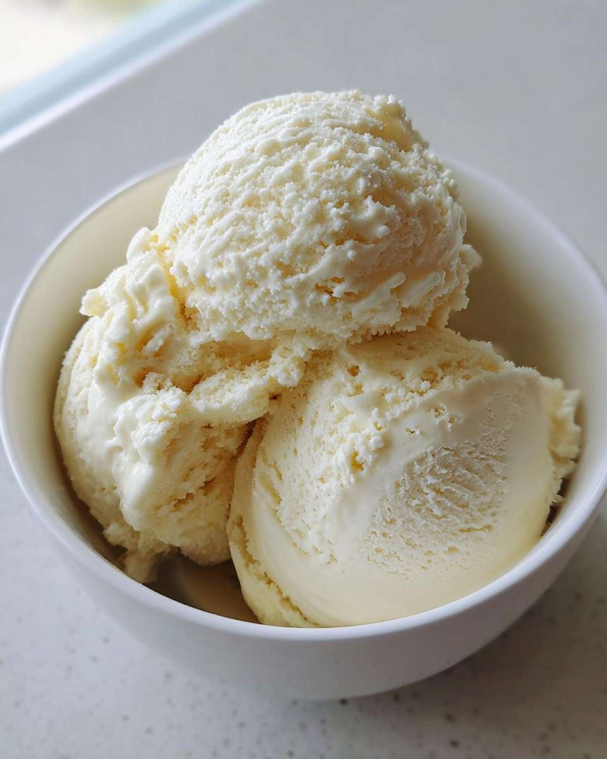 Three scoops of creamy, vanilla-colored protein ice cream served in a small white bowl.